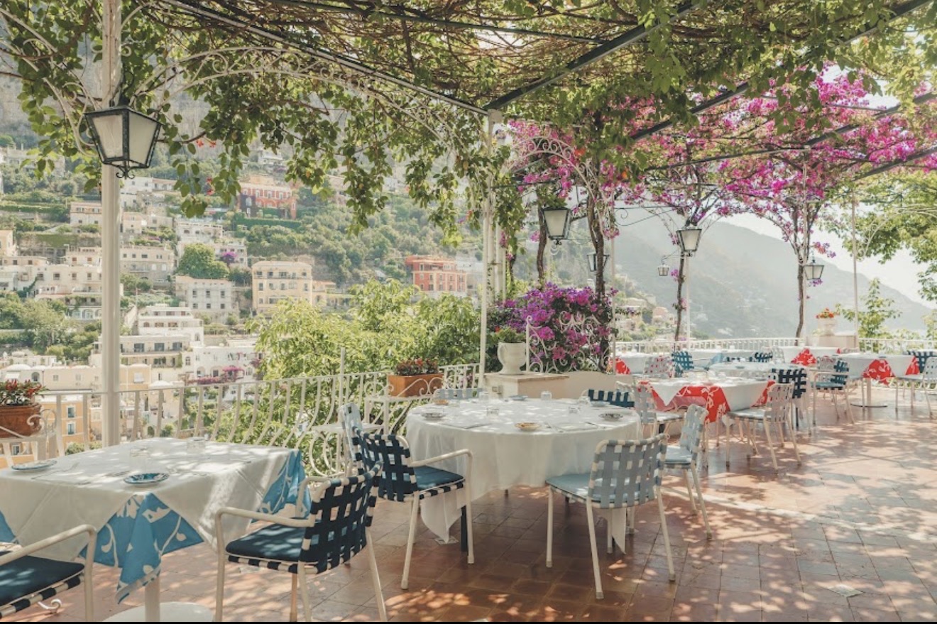 Il Tridente terrace dining with blue chairs, bougainvillea, and Positano views